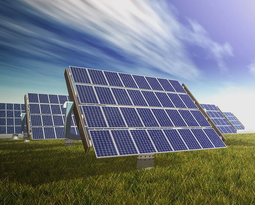 Rows of solar panels in a grassy field under a blue sky